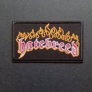 May include: A rectangular embroidered patch with a black background featuring the word hatebreed in red lettering with a white outline. Above the text is a stylized flame design in yellow and orange thread with a black border around the patch.