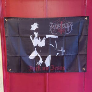 Könnte beinhalten: Schwarze Flagge mit einer weißen Grafik einer Person und dem Text "Fuck me Jesus". Die Flagge hat auch den Bandnamen "Marduk" in einer gotischen Schrift. Die Flagge hat Ösen in jeder Ecke.