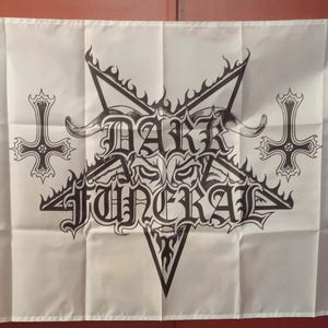 May include: White flag featuring a black pentagram with the words "DARK FUNERAL" in gothic lettering. Two inverted crosses flank the central design. The flag has gold grommets.