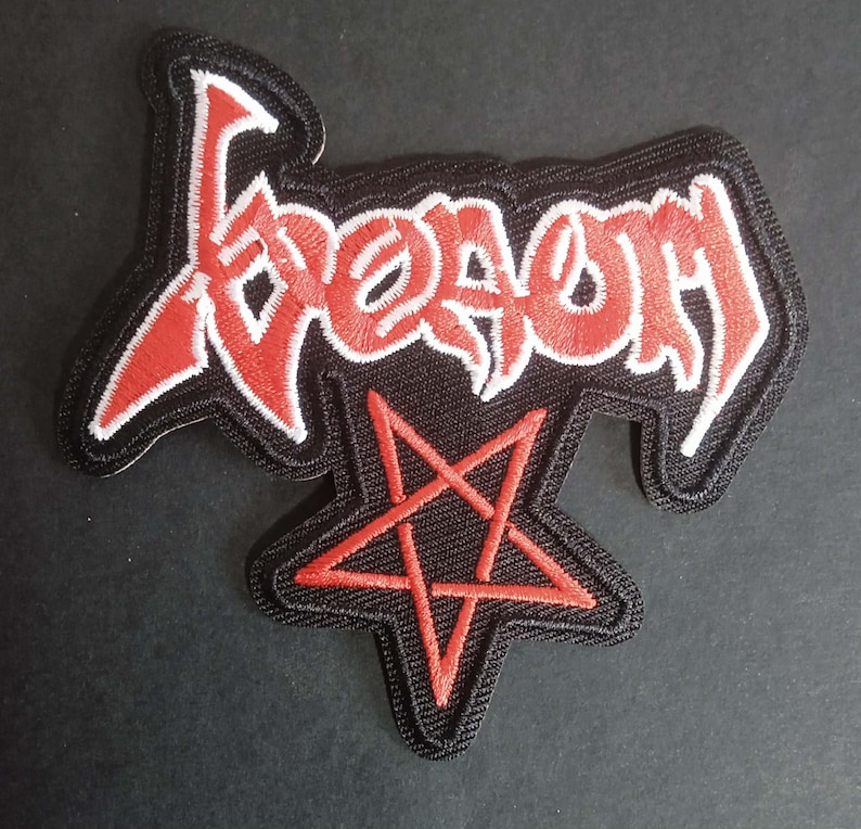 May include: Embroidered patch with the word "Venom" in red gothic lettering with a white outline, on a black background. A red pentagram is below the word. The patch has a black border.