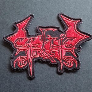 Può includere: Una toppa ricamata nera e rossa che presenta il testo Celtic Frost in un carattere stilizzato e frastagliato. Il design include estensioni affilate a forma di ala su entrambi i lati e dettagli intricati e appuntiti nelle lettere, il tutto bordato di nero.