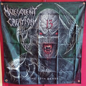 May include: A rectangular fabric wall banner featuring the Malevolent Creation logo in white text at the top left. The central graphic depicts a monstrous creature with red eyes, sharp teeth, and a red number 13 on its forehead. The text THE 13TH BEAST is printed in white at the bottom.