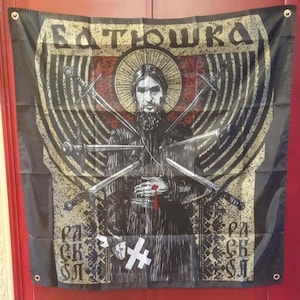 May include: Black flag featuring a religious figure with swords piercing his body. The figure has a halo and is surrounded by text in a stylized font. The flag has grommets for hanging.