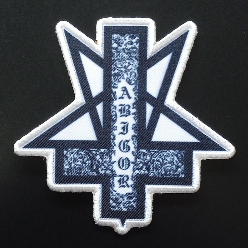 Puede incluir: Un parche bordado en blanco y negro con un dise&ntilde;o de pentagrama invertido estilizado. La barra vertical central contiene el texto ABIGOR en una fuente g&oacute;tica, rodeado de intrincados patrones florales. Toda la forma tiene un borde blanco.