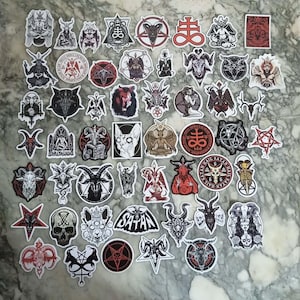 Puede incluir: Una colección de pegatinas con imágenes ocultas y satánicas. Las pegatinas presentan ilustraciones de demonios, pentagramas y otros símbolos relacionados en negro, blanco y rojo. Están dispuestas sobre una superficie de mármol.