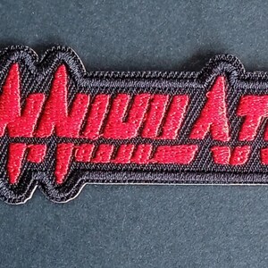 May include: A rectangular embroidered patch with a black background and a red border. The word ANNIHILATOR is stitched in red thread across the center in a stylized, jagged font that resembles a heartbeat monitor line or sound wave pattern.