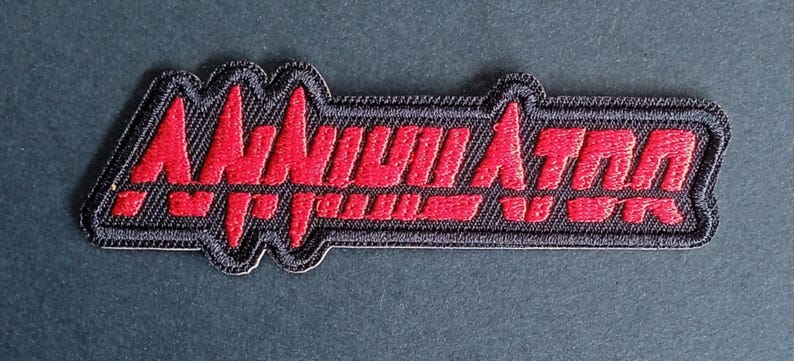 May include: A rectangular embroidered patch with a black background and a red border. The word ANNIHILATOR is stitched in red thread across the center in a stylized, jagged font that resembles a heartbeat monitor line or sound wave pattern.