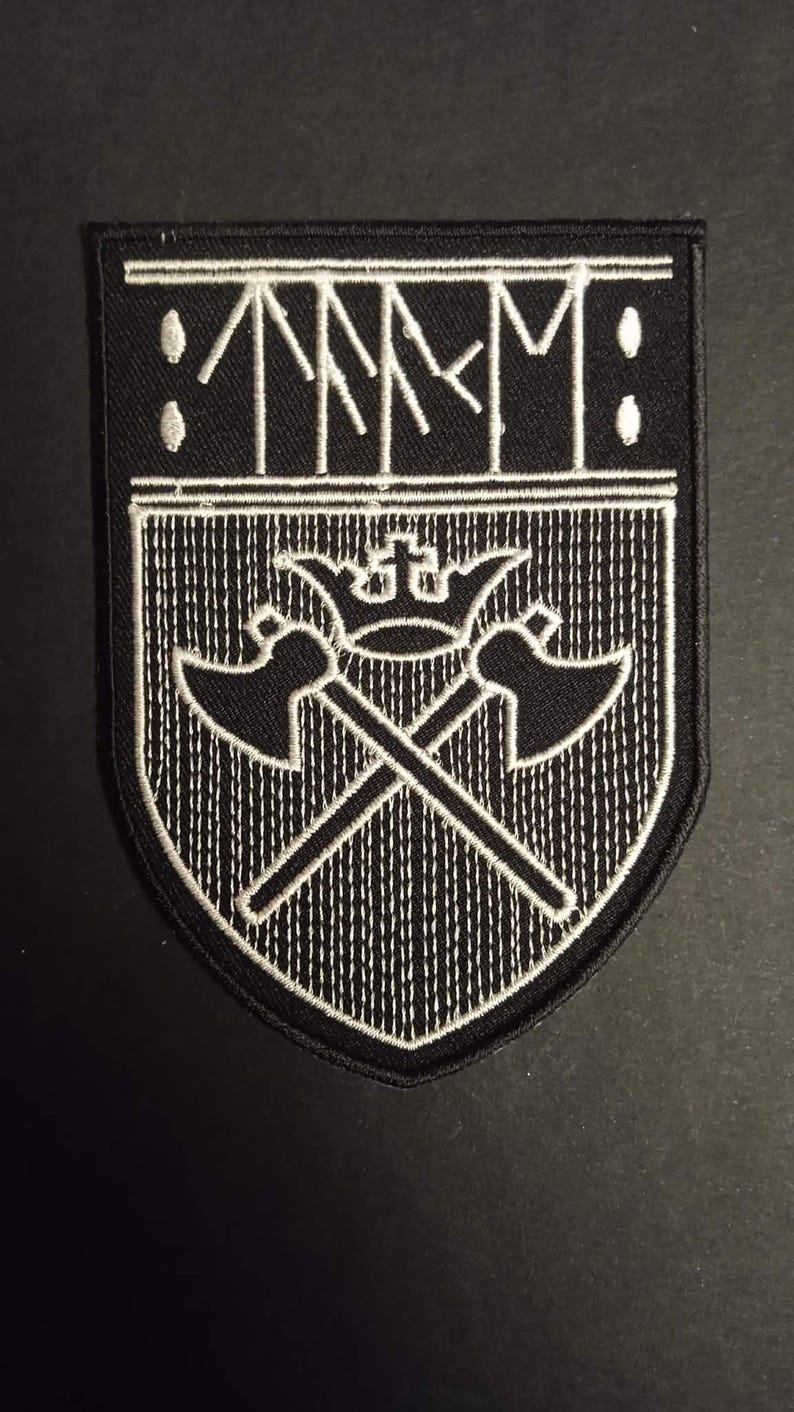 May include: Black and white embroidered patch with a shield design. The patch features the letters "TMM" above a crossed axe design with a crown. The patch is bordered in white stitching.