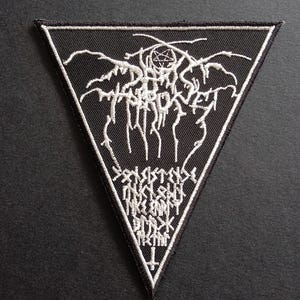 Op de afbeelding: Een driehoekige zwarte geborduurde patch met witte draaddetails. Het ontwerp bevat de tekst Darkthrone in een gestileerd lettertype, een pentagram, extra onleesbare tekst en een omgekeerd kruis op het onderste punt van de driehoek.