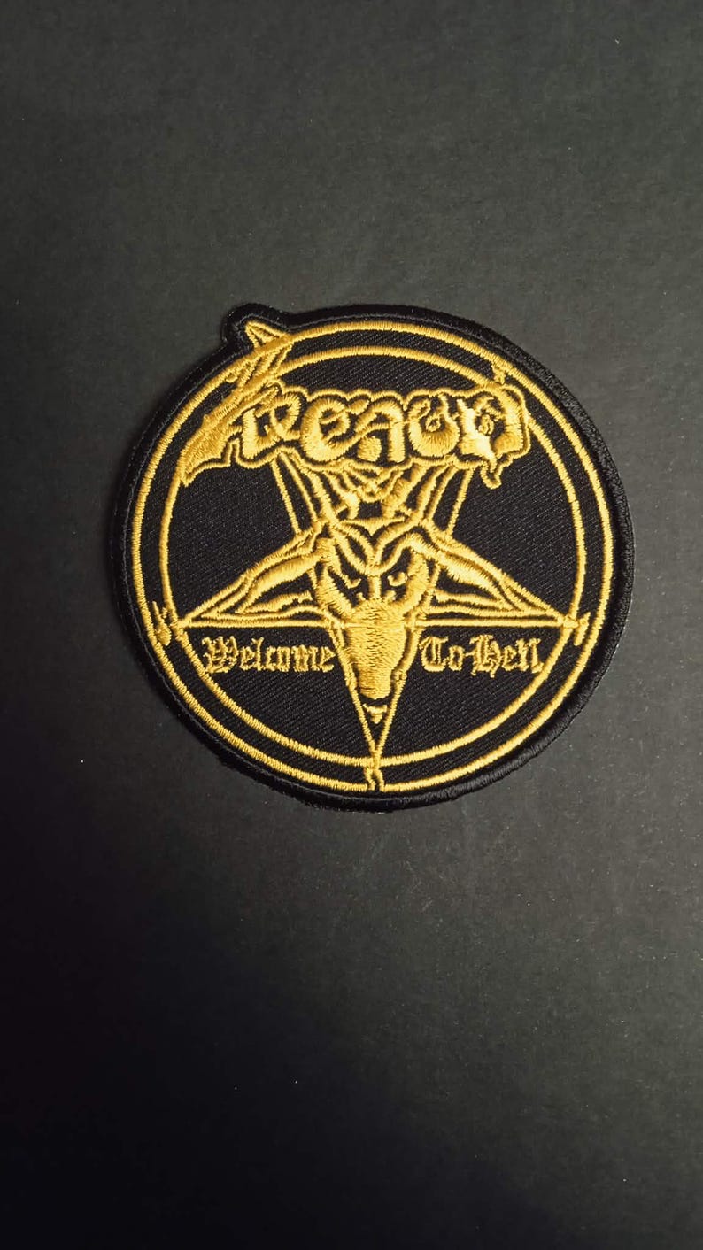 Może przedstawiać: Czarna i złota naszywka z haftem przedstawiająca pentagram z głową kozła pośrodku. Naszywka zawiera napis "Venom" u g&oacute;ry i "Welcome To Hell" na dole, wszystko złotymi literami.