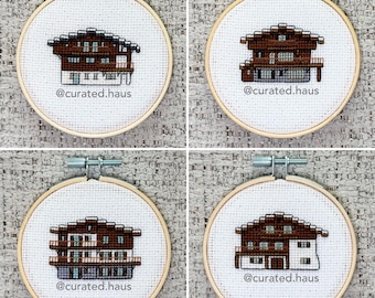 Peut inclure: Quatre tambours à broder circulaires en bois contenant du tissu Aida blanc avec des motifs au point de croix de maisons de style alpin marron et blanc. Chaque pièce présente le texte @curated.haus brodé en fil noir sous l'illustration.