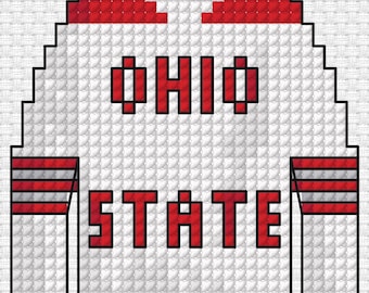 Peut inclure: Un maillot blanc à manches longues avec des accents rouges sur les épaules et les manches, doté de rayures rouges sur les poignets. Le texte OHIO STATE est imprimé en lettres rouges en style point de croix pixelisé sur le devant.