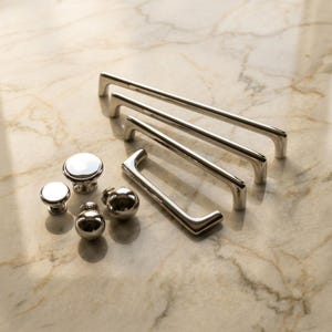 May include: A collection of polished silver-toned hardware including three rectangular cabinet pulls of varying lengths and four round cabinet knobs. The metal pieces feature a smooth, reflective finish and clean, simple lines for furniture.