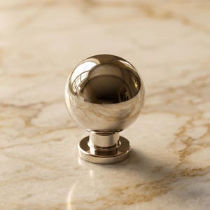 May include: A polished metallic cabinet knob featuring a spherical head and a cylindrical base. The surface of the knob is highly reflective, showing a clear mirror-like finish that captures light and surrounding shapes in its smooth, rounded form.