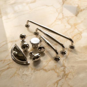 May include: A collection of polished silver-toned cabinet hardware including three long arched drawer pulls, one semi-circular cup pull, and four round knobs of varying sizes. Each piece features a smooth, reflective metallic finish.