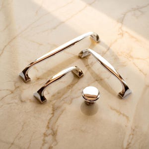May include: A collection of polished chrome cabinet hardware consisting of one long drawer pull, one medium drawer pull, one short drawer pull, and one round cabinet knob. Each piece features a smooth, reflective metallic finish and curved design.