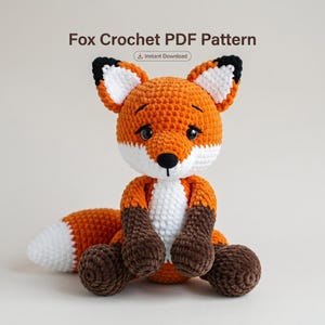 Op de afbeelding: Een gehaakte vossenpop met oranje, witte en bruine draad. De vos heeft een witte borst, een witgepunte staart en zwarte accenten op de oren. De tekst "Fox Crochet PDF Pattern" staat bovenaan de afbeelding.