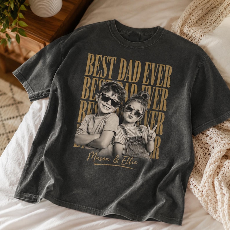 May include: Dark gray t-shirt with the text "BEST DAD EVER" in gold lettering. The shirt features a black and white photo of two children wearing sunglasses. The names "Mason & Ellie" are printed below the photo.