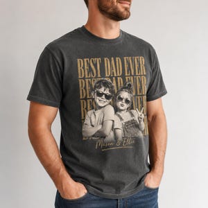 May include: Dark gray t-shirt with the text "BEST DAD EVER" in gold lettering. The shirt features a sepia-toned photo of two children wearing sunglasses. The children's names, Mason & Ellie, are printed below the photo.