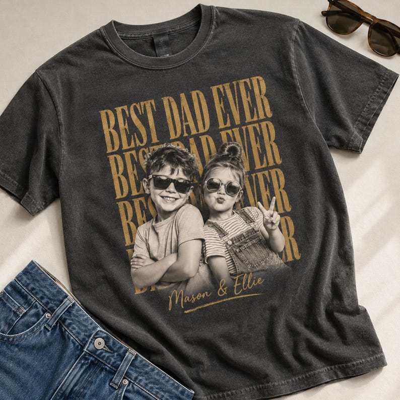May include: Dark gray t-shirt with the text "BEST DAD EVER" in gold lettering. The shirt features a sepia-toned photo of two children wearing sunglasses. The names "Mason & Ellie" are printed below the photo.