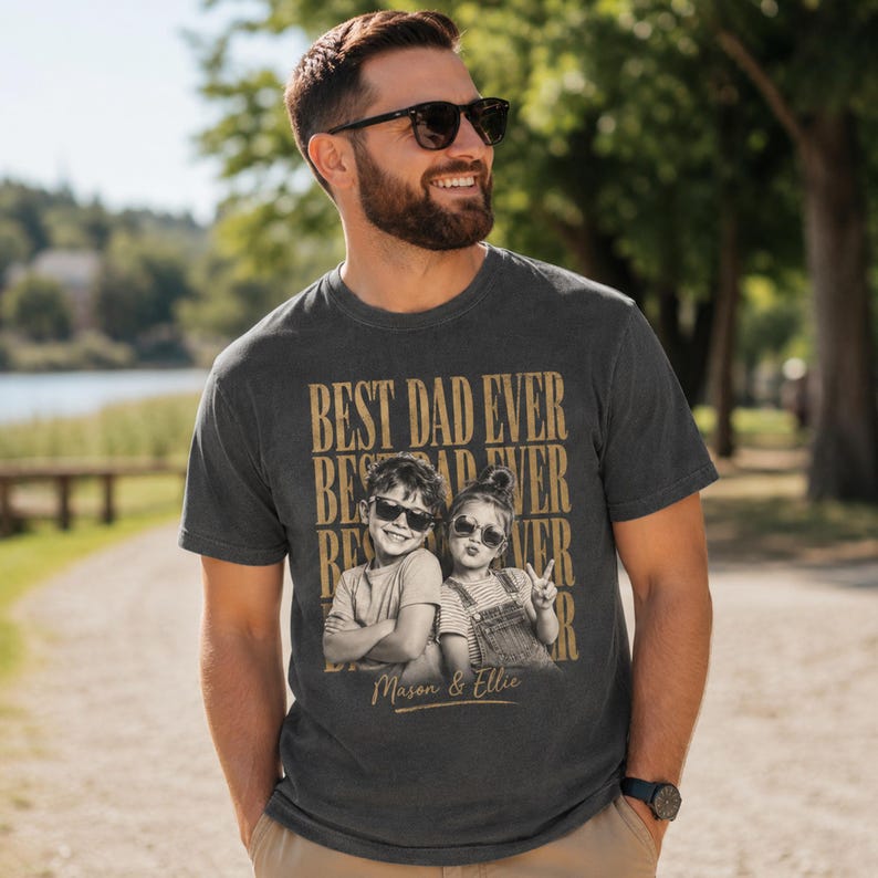 May include: Dark gray t-shirt with the text "BEST DAD EVER" in a stacked design. The shirt features a black and white photo of two children wearing sunglasses. The names "Mason & Ellie" are printed below the photo.