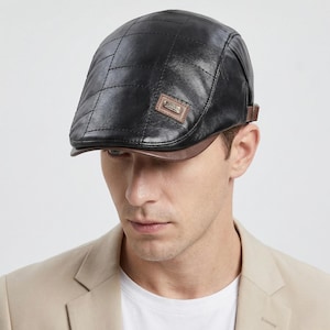 May include: Black leather flat cap with a quilted design. The cap features a brown brim and a small rectangular label with text. A brown strap is on the side. The cap is worn by a person.