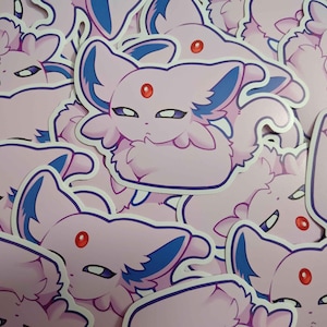 May include: A collection of stickers featuring a cartoon Espeon character. The stickers are primarily pink with blue accents on the ears and tail. Each sticker has a red gem on its forehead and a white outline.