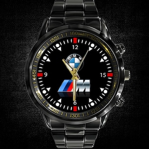 Pode incluir: Relógio de pulso preto com bracelete e mostrador pretos. O mostrador do relógio apresenta o logótipo da BMW, com detalhes brancos e vermelhos. O relógio tem ponteiros dourados e uma luneta dourada. O diâmetro da caixa é de cerca de 40 mm.