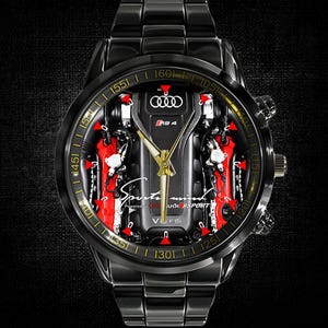 Puede incluir: Reloj de pulsera negro con una esfera detallada que presenta un diseño de motor de coche con detalles en rojo y plata. El reloj tiene una correa de metal negro y un bisel dorado con números. La esfera del reloj incluye el texto "Sports mind" y el logotipo de Audi.