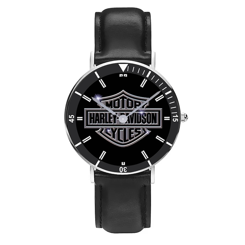 May include: A black wristwatch with a silver-colored bezel and a black leather band. The watch face features the Harley-Davidson logo in silver against a black background. The watch has white hour markers and hands.