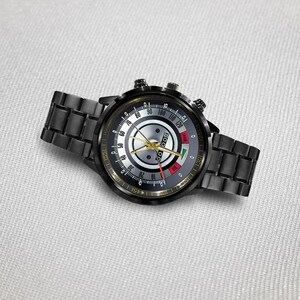 May include: Black wristwatch with a round face and a black metal band. The watch face features a silver center with black and yellow markings, and a red and green indicator. The watch has two small dials on the side.