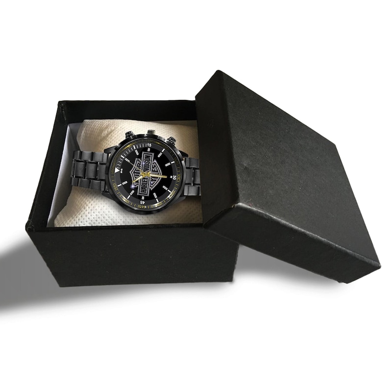 May include: Black wristwatch with a Harley-Davidson logo on the face, presented in an open black gift box. The watch has a black metal band and a gold-colored bezel. The watch face is black with gold accents.
