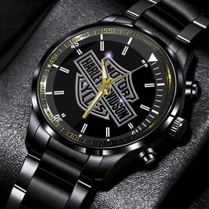 May include: Black wristwatch with a stainless steel band. The watch face is black with gold accents and the Harley-Davidson logo. The watch has a chronograph design and a date display.