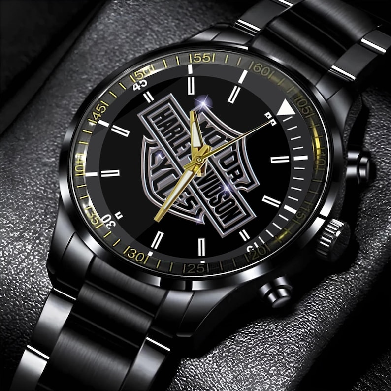 May include: Black wristwatch with a stainless steel band. The watch face is black with gold accents and the Harley-Davidson logo. The watch has a chronograph design and a date display.