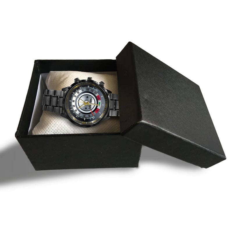 May include: A black wristwatch with a silver and gold face, presented in a black gift box. The watch features a metallic band and a detailed dial with multiple sub-dials and hands. The box is open, revealing the watch resting on a white cushion.