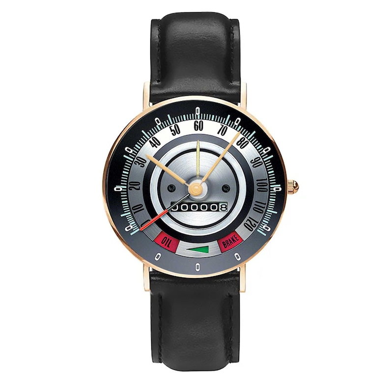 May include: A wristwatch with a black leather band and a gold-colored case. The watch face resembles a car speedometer, with a black and silver dial, gold hands, and the word "BRAKE".