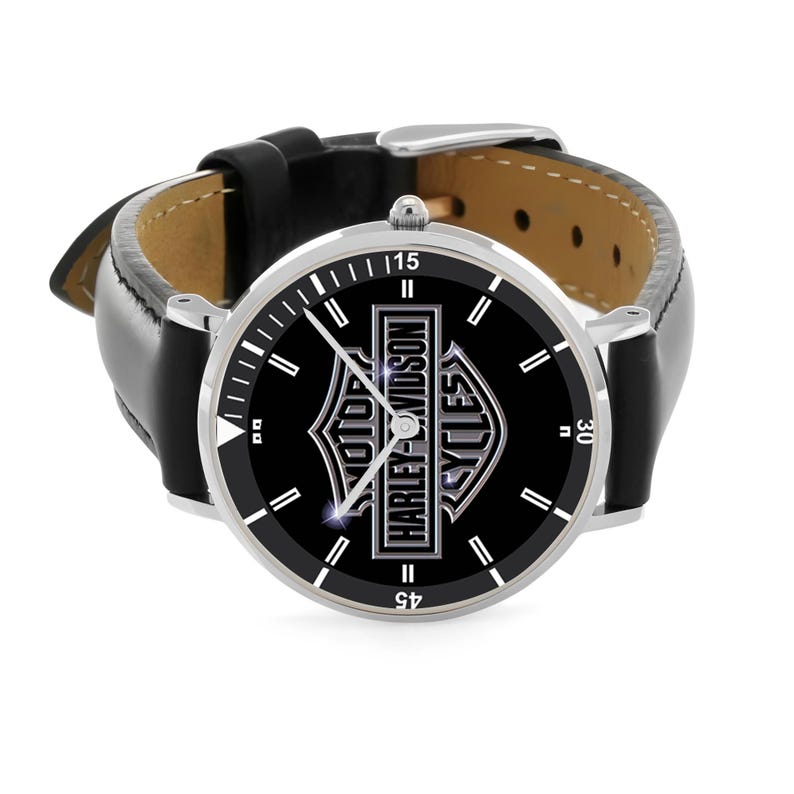 May include: A silver-toned wristwatch with a black face featuring the Harley-Davidson logo. The watch has a black leather band and a silver bezel with white markers. The watch face displays the text "HARLEY-DAVIDSON CYCLES".