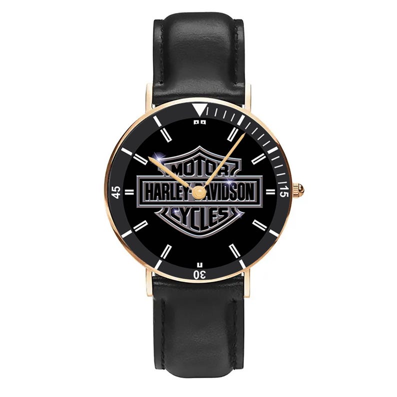 May include: A black watch with a gold-colored bezel and a black leather band. The watch face features the Harley-Davidson logo in silver against a black background. The watch has white markers and hands.