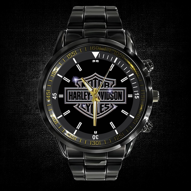 May include: Black wristwatch with a stainless steel band and a black face. The watch face features the Harley-Davidson logo in silver and gold, with gold hands and markers. The watch has a chronograph design.