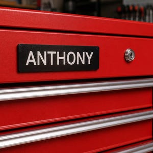 May include: A red metal tool chest with multiple drawers and silver handles. A black nameplate with the name "ANTHONY" in white lettering is affixed to the top drawer. A key lock is visible on the right side.