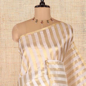 May include: A saree featuring alternating vertical stripes of white and metallic gold fabric. The garment is draped over a mannequin and is paired with a delicate gold-toned choker necklace adorned with small colorful beads and white accents.