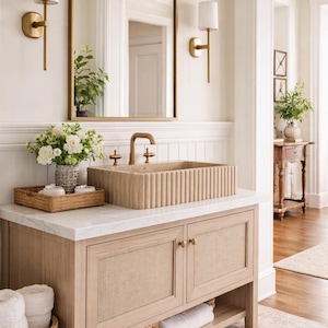 Può includere: Mobile da bagno in legno chiaro, con lavabo in pietra e specchio con cornice dorata. Il mobile ha ante in canna intrecciata e un piano in marmo. Applique decorative e un cesto intrecciato completano l'estetica della stanza.