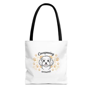 May include: White tote bag with black handles. The bag features a cartoon Cavapoo dog illustration, surrounded by paw prints and bones, with the text "Cavapooing around". A practical and stylish accessory.