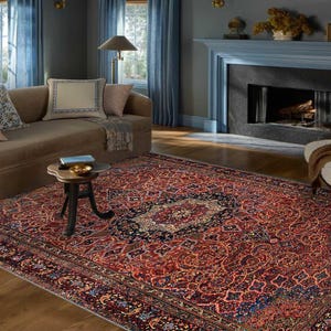 K&ouml;nnte beinhalten: Ein gro&szlig;er, rechteckiger persischer Teppich mit einem detaillierten Blumenmuster in Rot-, Blau- und Cremet&ouml;nen. Der Teppich befindet sich in einem Wohnzimmer, mit Sofa, Stuhl und Kamin im Hintergrund.