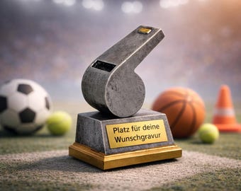 Op de afbeelding: Een metalen fluit-trofee op een rechthoekige basis met gouden rand. De basis heeft een gouden plaat met de tekst "Platz für deine Wunschgravur". Een voetbal, een basketbal, een tennisbal en een verkeerskegel staan op de achtergrond.