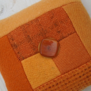 May include: A patchwork pincushion made of orange and brown fabric with a large amber button in the center.