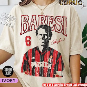 Könnte beinhalten: Ein elfenbeinfarbenes Kurzarm-T-Shirt mit einer verwaschenen Grafik eines Fußballspielers im rot-schwarz gestreiften Trikot, der Nummer 6 und dem Namen BARESI in großen roten Buchstaben über dem Porträt sowie einer Signatur rechts daneben.