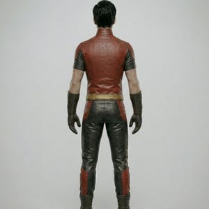 May include: A red and black costume with a high collar, short sleeves, and a gold belt. The pants are black with red accents. The costume includes gloves and boots. The person is facing away from the camera.
