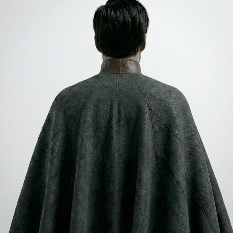 May include: A dark gray cape with a brown leather collar. The cape is made of a textured fabric and drapes over the shoulders. The person's back is facing the camera.