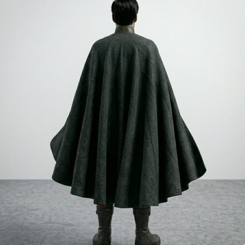 May include: A dark gray cape with a wide, flowing design. The cape is worn over a dark top and paired with matching boots. The person is seen from the back, standing on a gray tiled floor.